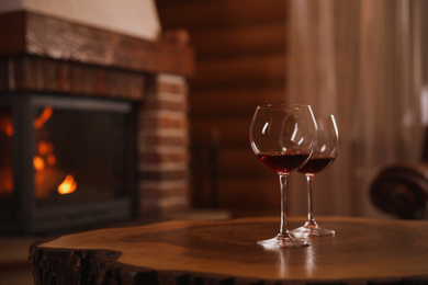 Photo of Glasses of red wine on wooden table near fireplace. Space for text