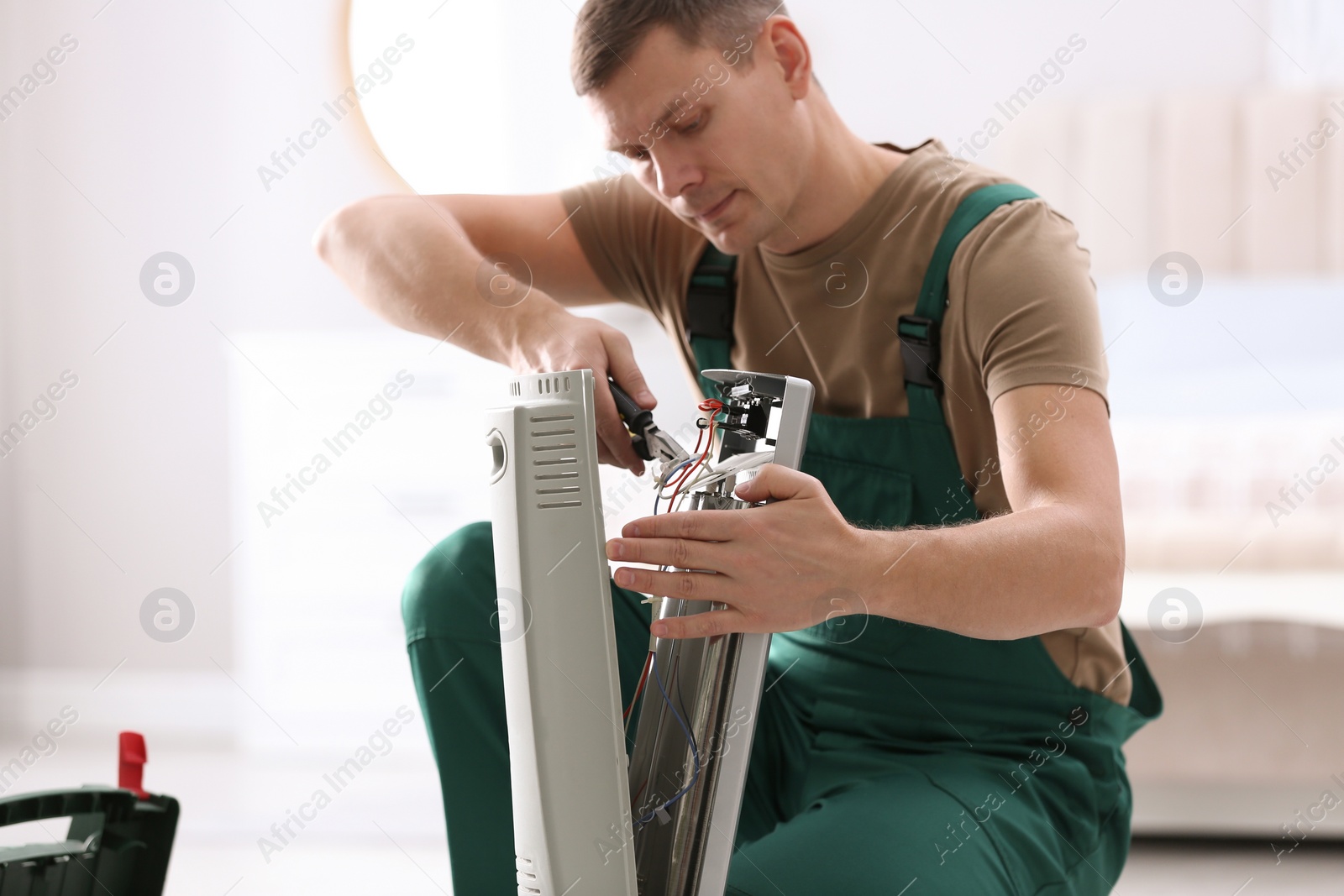 Photo of Professional technician repairing electric ultrared heater with pliers indoors