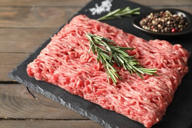 Raw ground meat, spices and rosemary on wooden table, closeup