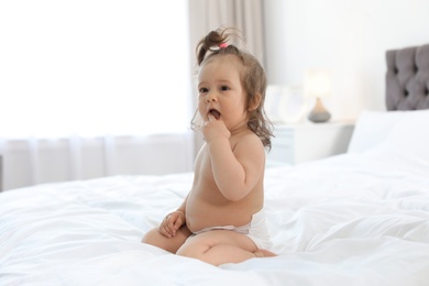 Adorable little baby girl sitting on bed in room