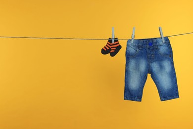 Photo of Baby pants and socks clothes drying on laundry line against orange background, space for text