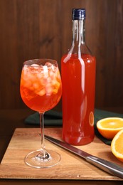 Photo of Aperol spritz cocktail and ice cubes in glass and bottle on wooden table