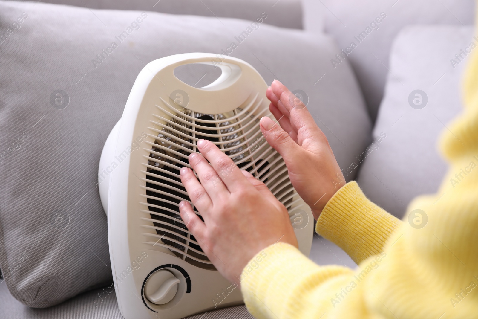 Photo of Woman warming hands near fan heater indoors, closeup