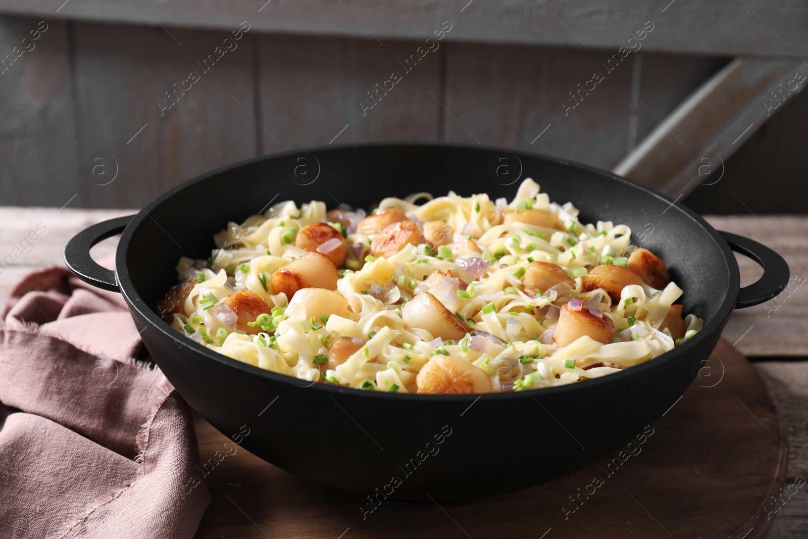 Photo of Delicious scallop pasta with onion in pan on table, closeup