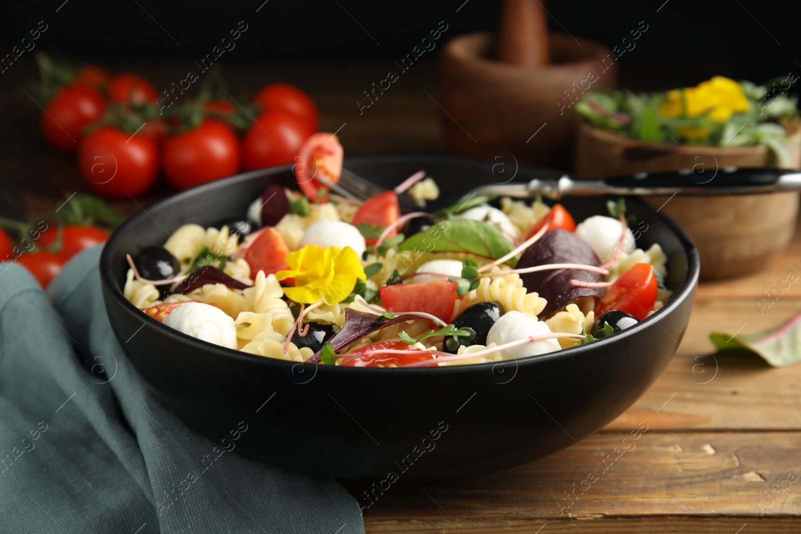 Photo of Bowl of delicious pasta with tomatoes, olives and mozzarella on wooden table, closeup