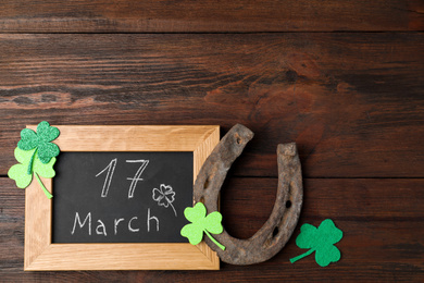 Photo of Flat lay composition with horseshoe and chalkboard on wooden background, space for text. St. Patrick's Day celebration