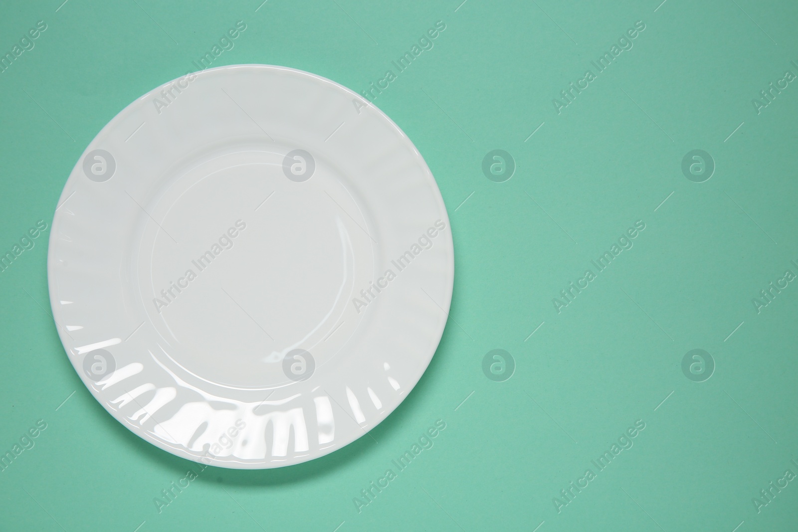 Photo of One white plate on turquoise background, top view. Space for text