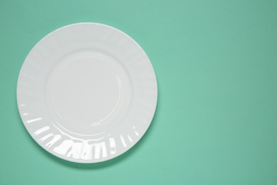 Photo of One white plate on turquoise background, top view. Space for text