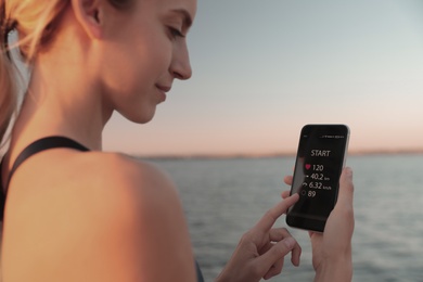 Young woman using fitness app on smartphone near river at sunset, closeup