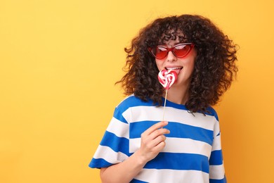 Photo of Beautiful woman in sunglasses with lollipop on yellow background, space for text