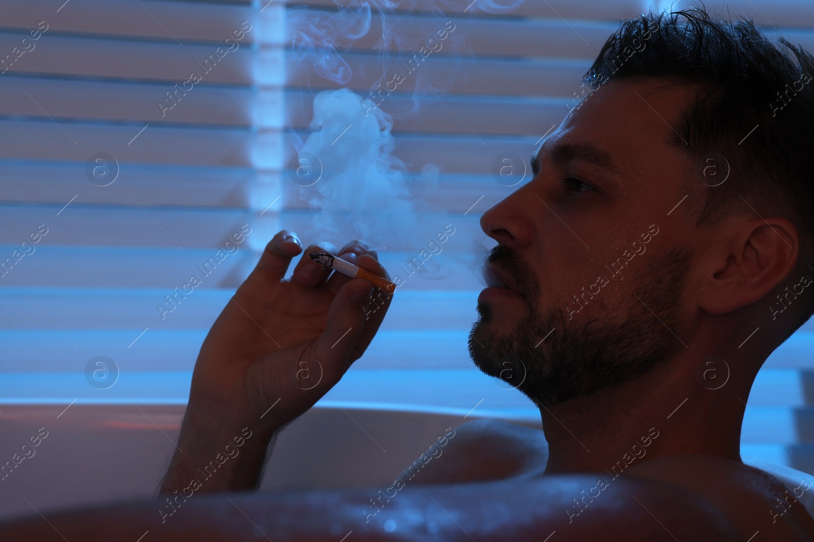 Photo of Upset man smoking in bathtub at night. Loneliness concept