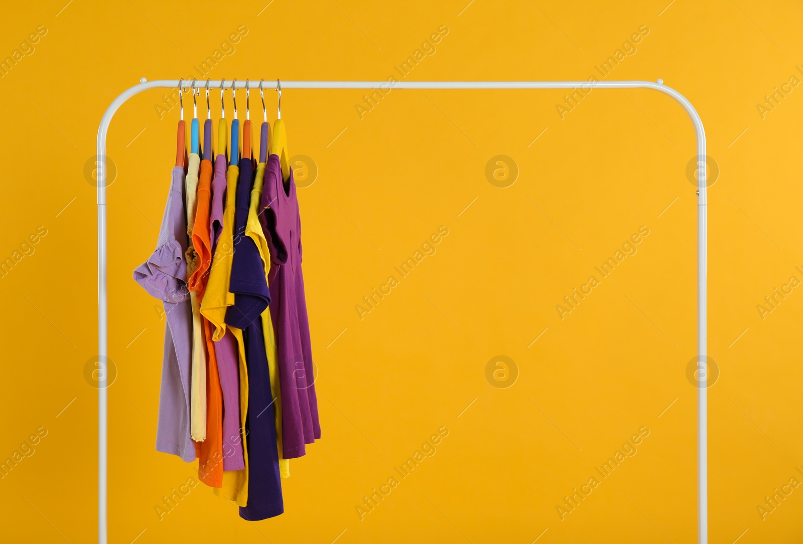 Photo of Rack with stylish children clothes on yellow background