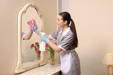 Photo of Young chambermaid cleaning dressing table in hotel room