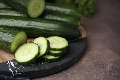 Photo of Fresh whole and cut cucumbers on brown textured table, closeup