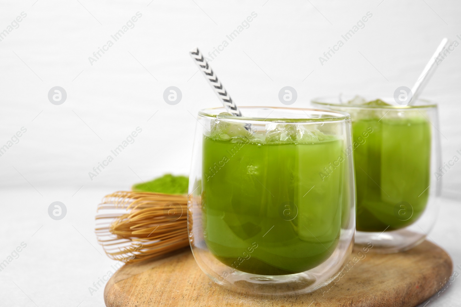 Photo of Delicious iced green matcha tea and bamboo whisk on white table, closeup. Space for text