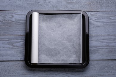 Photo of Roll of parchment paper with baking pan on grey wooden table, top view