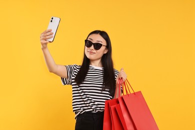 Beautiful woman with shopping bags taking selfie on yellow background