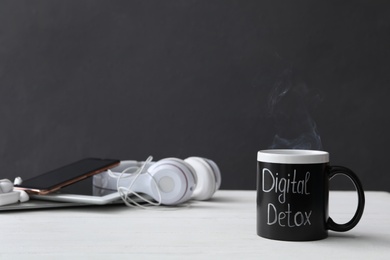 Photo of Different gadgets and cup with words DIGITAL DETOX on white wooden table