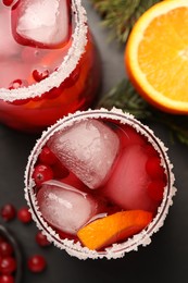 Tasty cranberry cocktail with ice cubes in glasses on dark gray table, flat lay