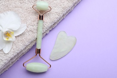 Gua sha stone, face roller, towel and orchid flower on violet background, flat lay. Space for text