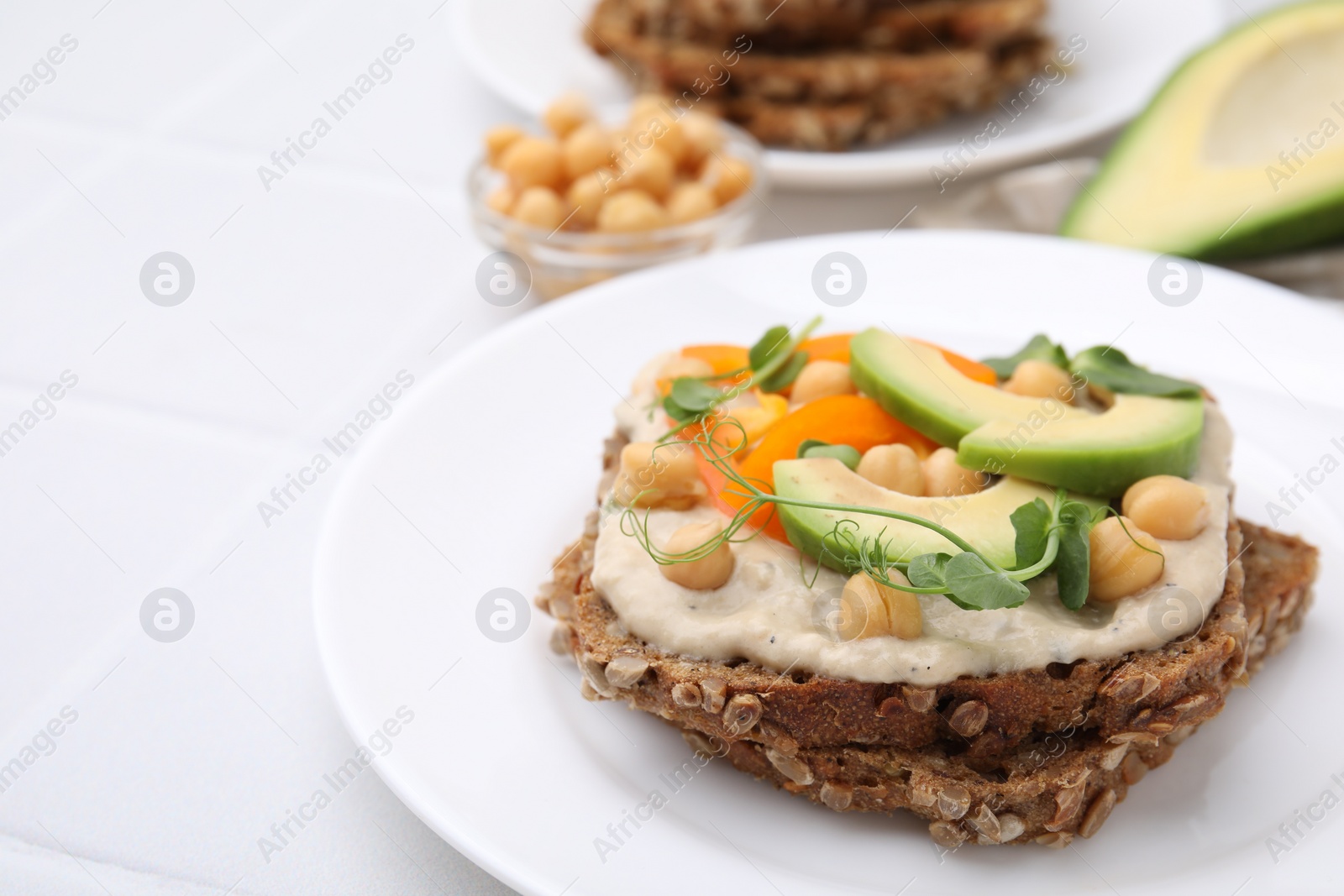 Photo of Tasty vegan sandwich with avocado, chickpeas and bell pepper on white table, closeup