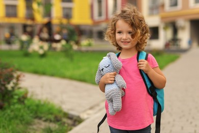Photo of Little girl with toy walking to kindergarten outdoors. Space for text