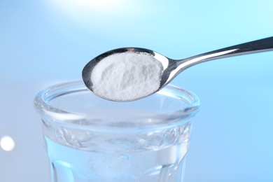 Photo of Adding baking soda into glass of water on light blue background, closeup