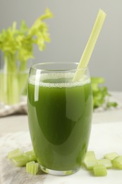 Glass of celery juice and fresh vegetables on light table, closeup