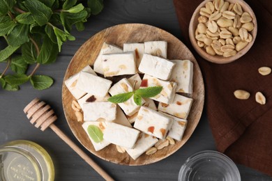 Photo of Pieces of delicious nutty nougat, peanuts, mint and honey on gray wooden table, flat lay