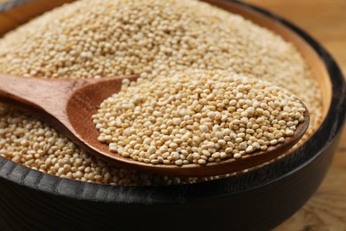 Photo of Dry quinoa seeds and spoon in bowl on table, closeup