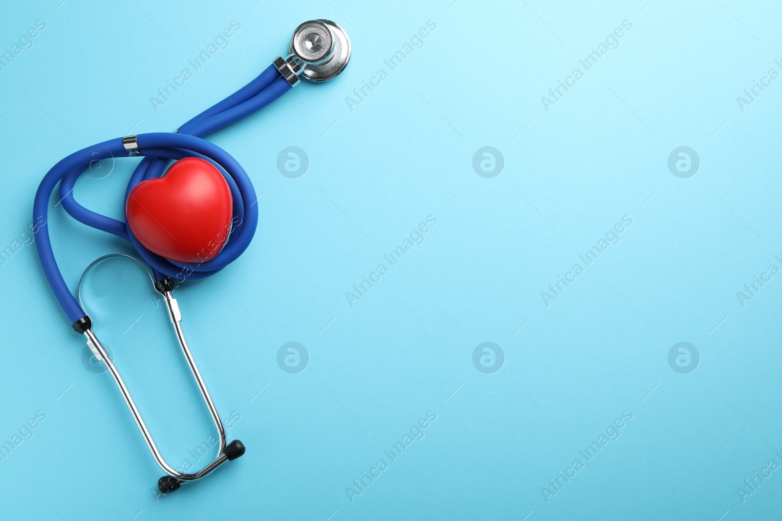 Photo of Stethoscope and red heart on light blue background, top view. Space for text