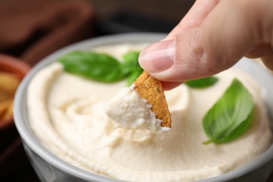 Photo of Woman dipping crunchy snack into delicious tofu sauce, closeup