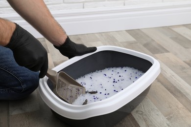 Photo of Man in gloves cleaning cat litter tray at home, closeup