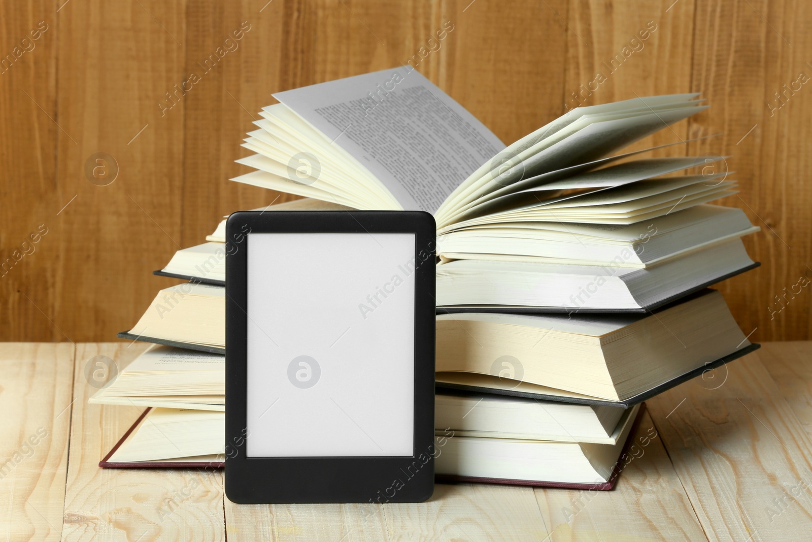 Photo of Portable e-book reader and open hardcover books on wooden table