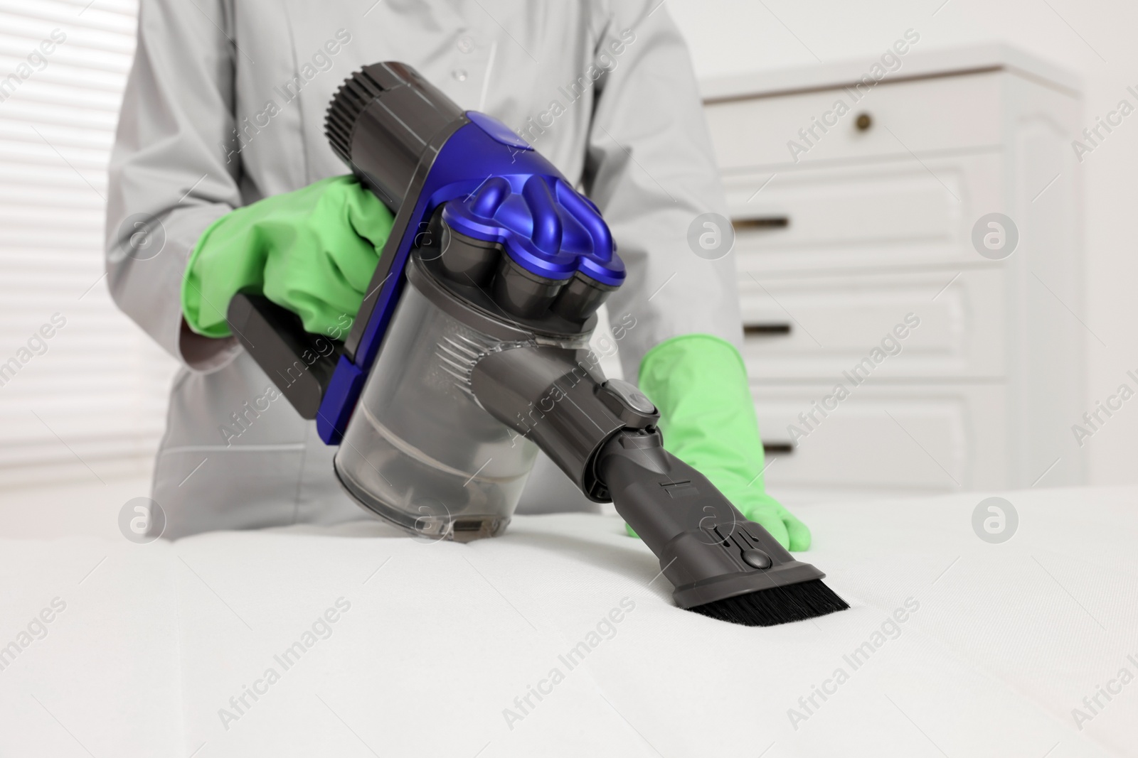 Photo of Woman in gloves disinfecting mattress with vacuum cleaner indoors, closeup