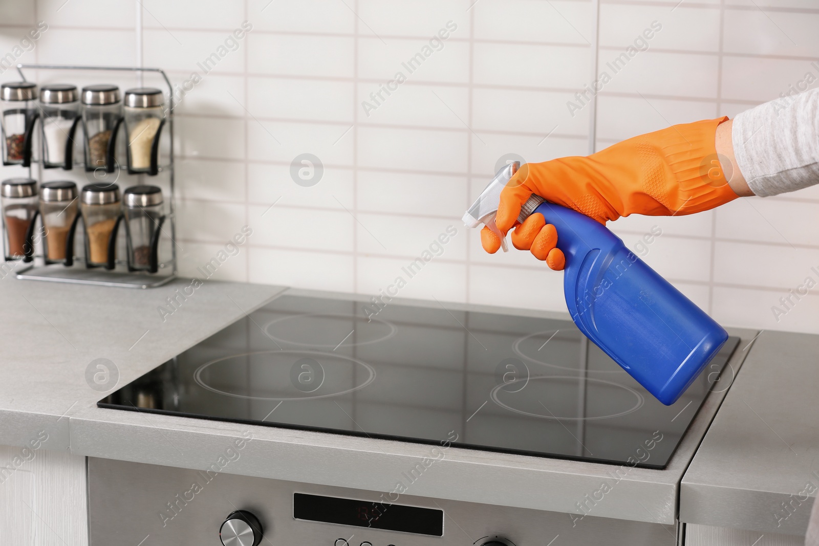 Photo of Woman cleaning stove with detergent in kitchen, closeup