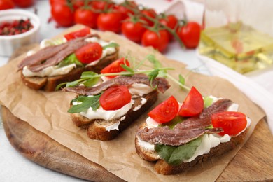 Photo of Delicious bruschettas with anchovies, tomatoes, microgreens and cream cheese on white table, closeup