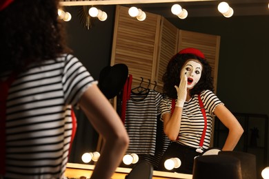 Photo of Young woman in mime costume posing near mirror indoors