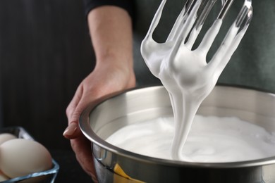 Photo of Woman making whipped cream with hand mixer on black background, closeup