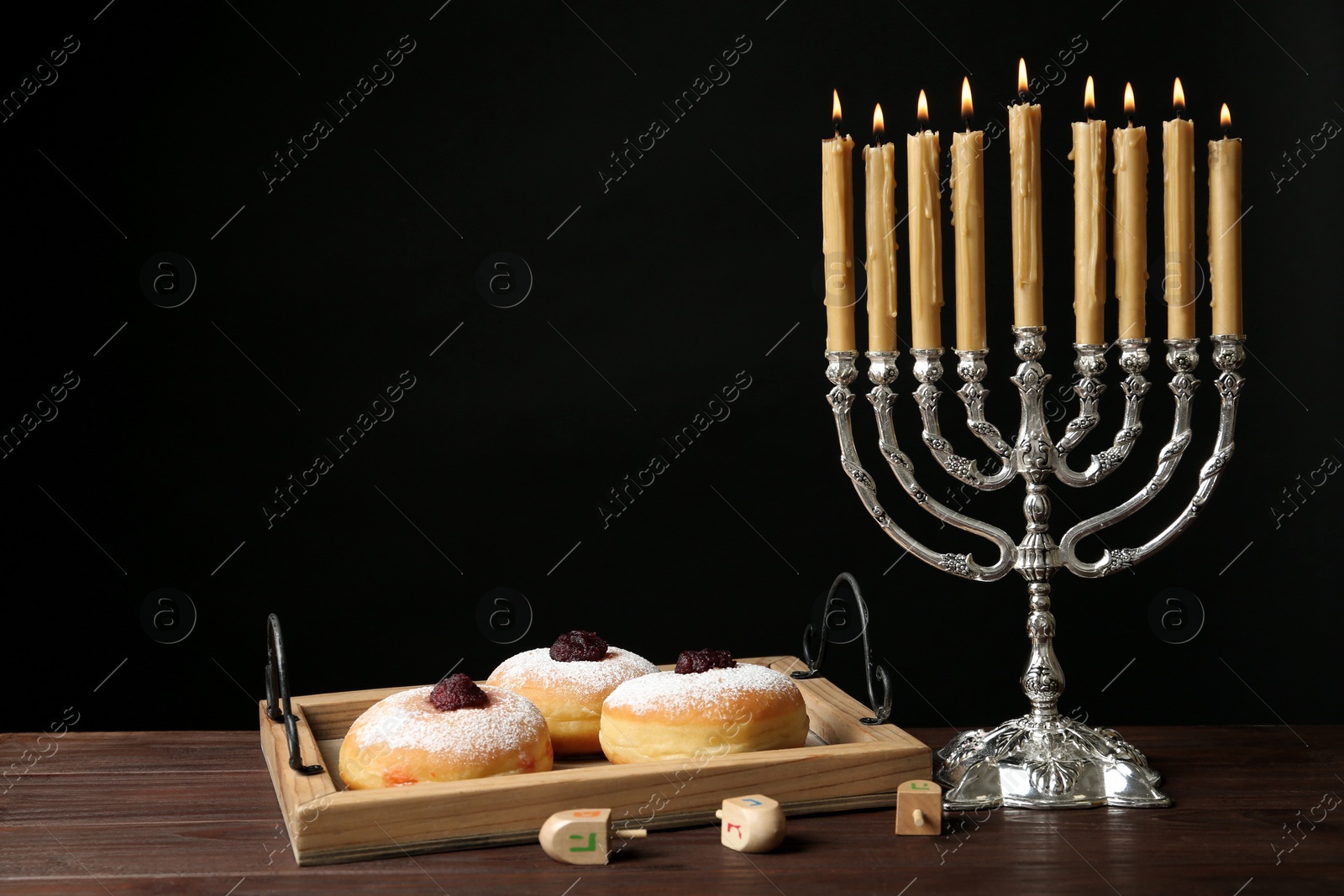 Photo of Silver menorah near sufganiyot and dreidels with symbols Nun, He, Pe, Gimel on black background. Space for text