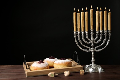 Photo of Silver menorah near sufganiyot and dreidels with symbols Nun, He, Pe, Gimel on black background. Space for text