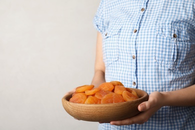 Photo of Woman holding plate with dried apricots on light background, space for text. Healthy fruit