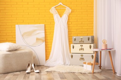 Stylish room interior with storage trunks, ottoman and beautiful wedding dress near yellow brick wall