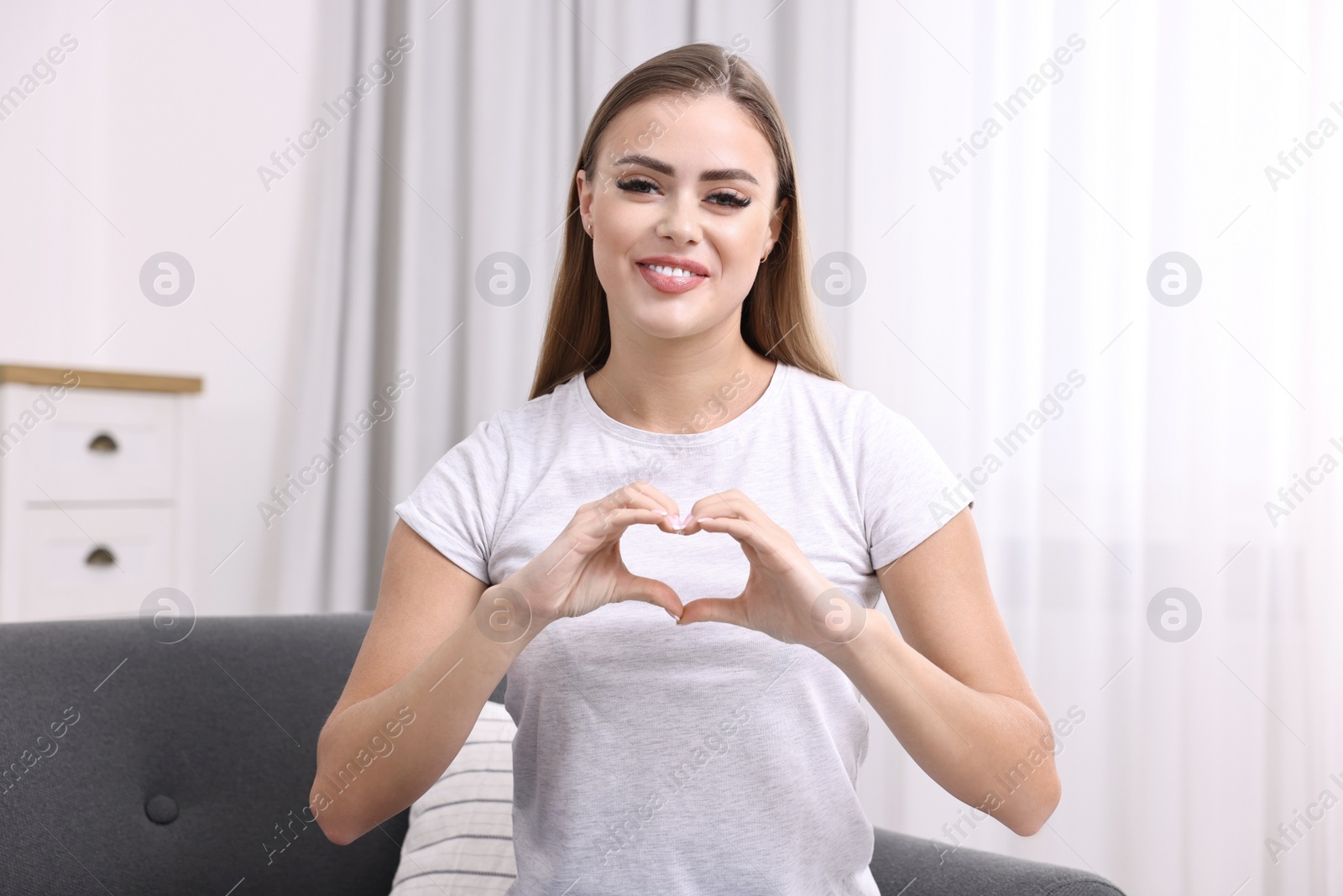 Photo of Happy woman showing heart gesture with hands at home