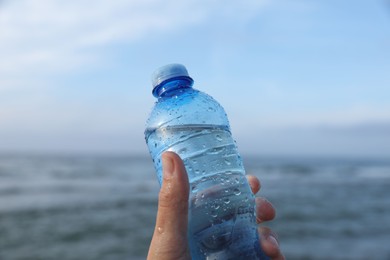 Photo of Woman holding plastic bottle with water near sea, closeup