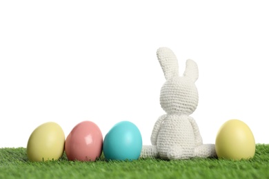 Cute Easter bunny toy and dyed eggs on green grass against white background, space for text