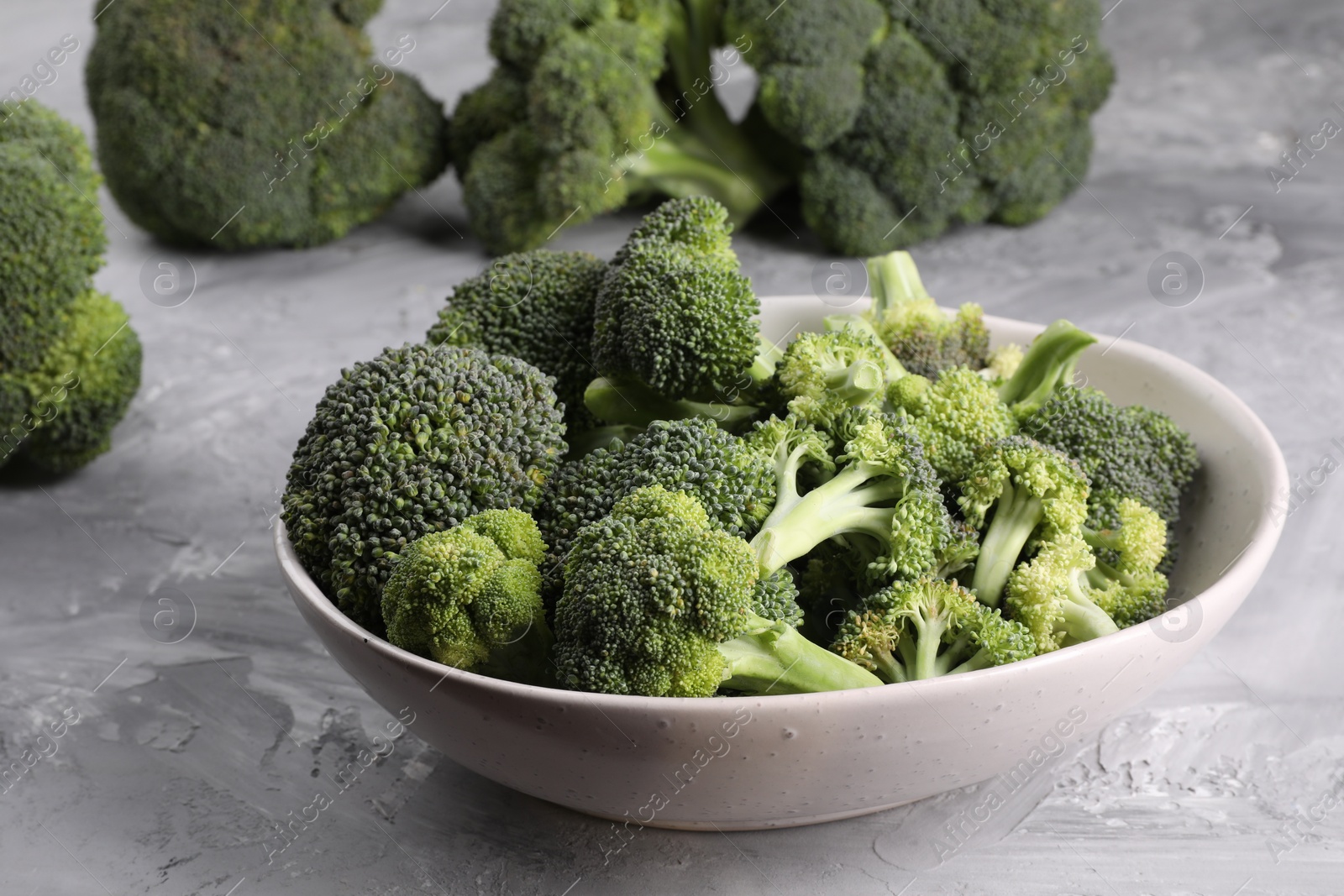 Photo of Bowl of fresh raw broccoli on grey textured table