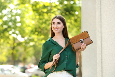 Photo of Beautiful young woman with stylish leather bag outdoors on summer day