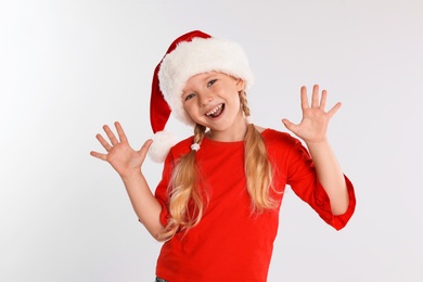 Photo of Happy little child in Santa hat on light grey background. Christmas celebration