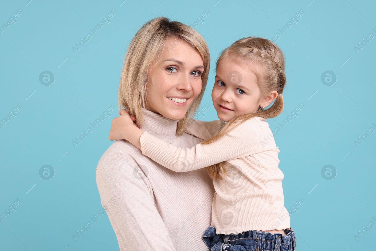 Photo of Daughter hugging her happy mother on light blue background